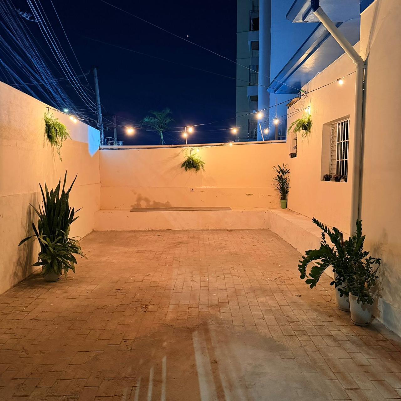 Pátio externo com plantas e luzes acesas ao entardecer