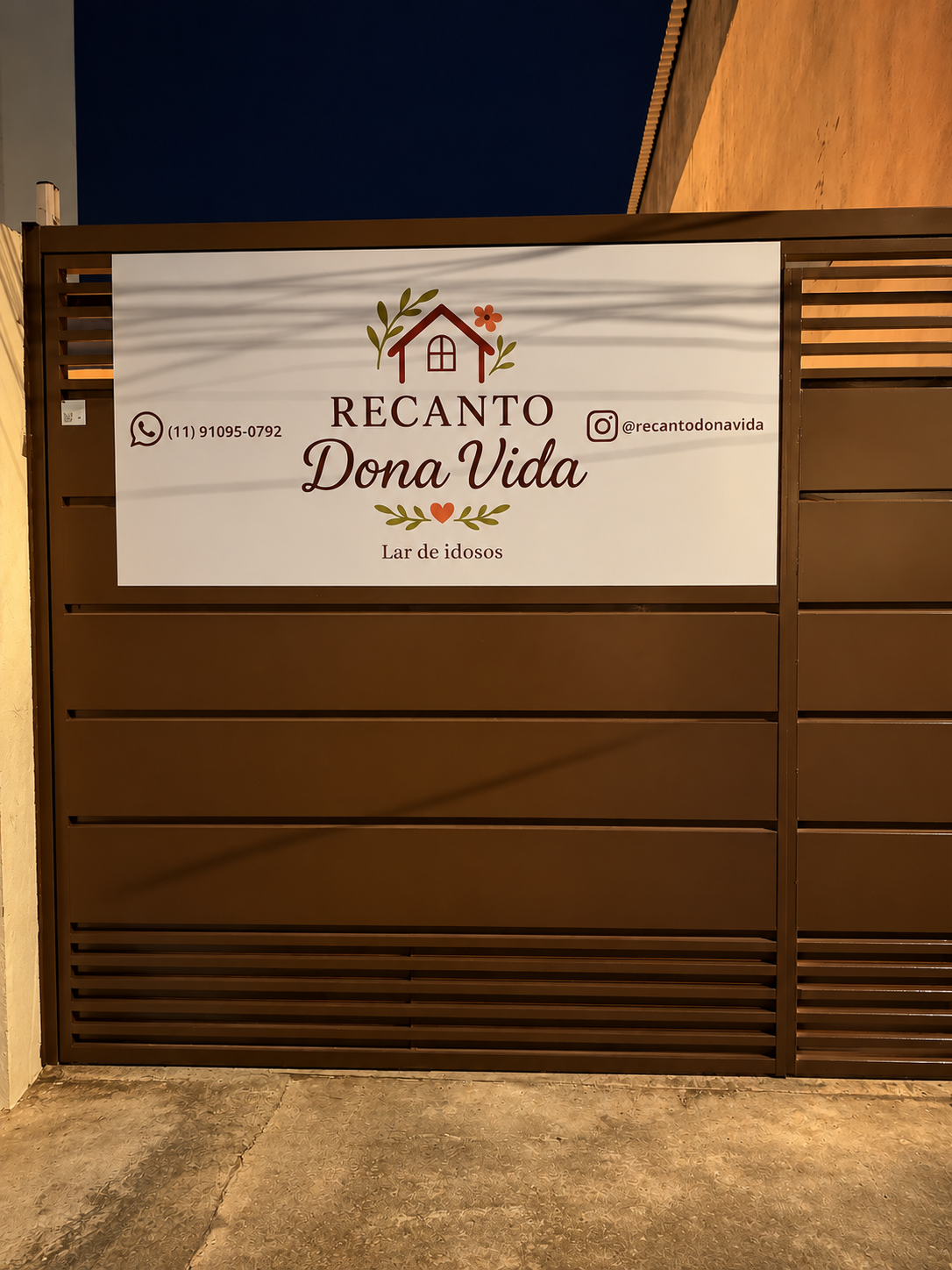 Portão do Recanto Dona Vida à noite, com a placa da casa